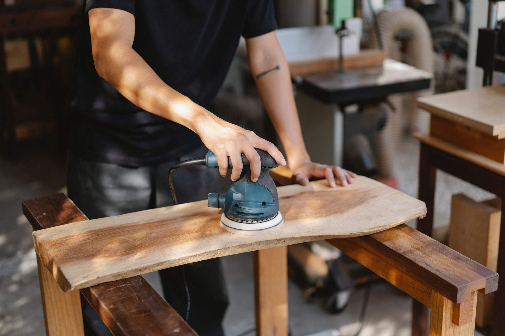 A craftsman sanding a curved piece of timber on a workbench